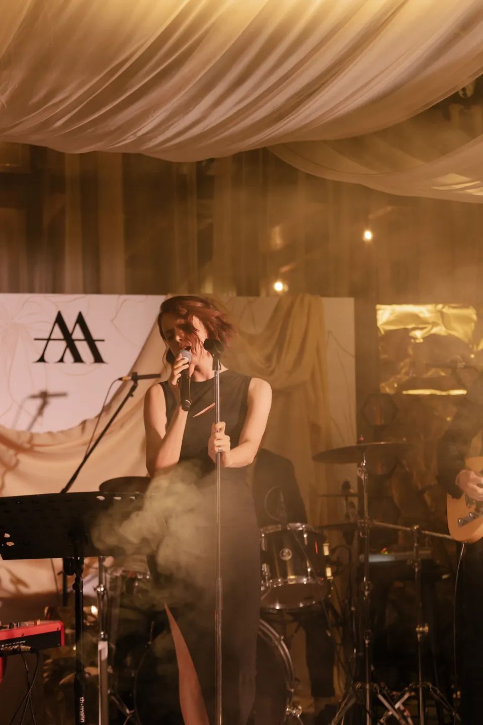 Live vocalist on a draped stage with monogrammed backdrop and smoke — evening reception