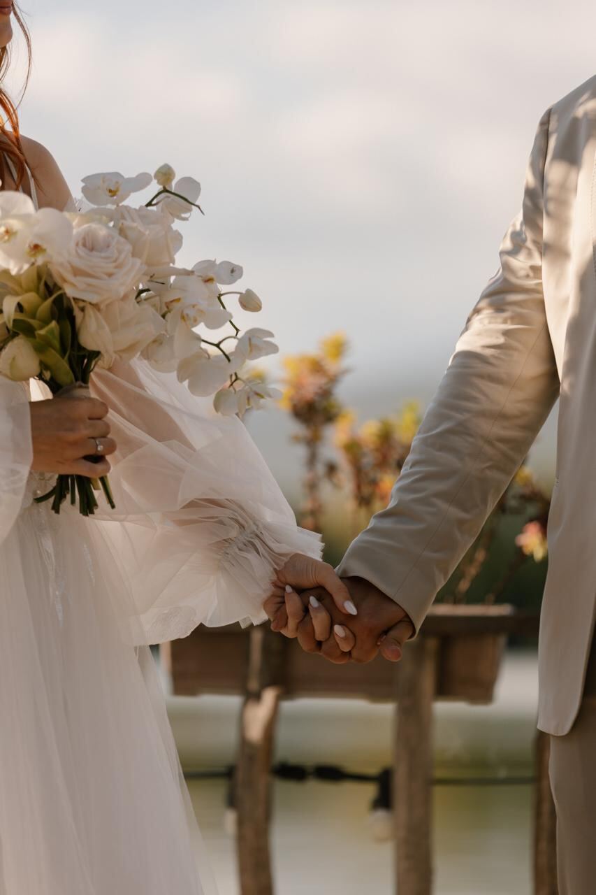 Close-up of bride and groom holding hands with an orchid bouquet