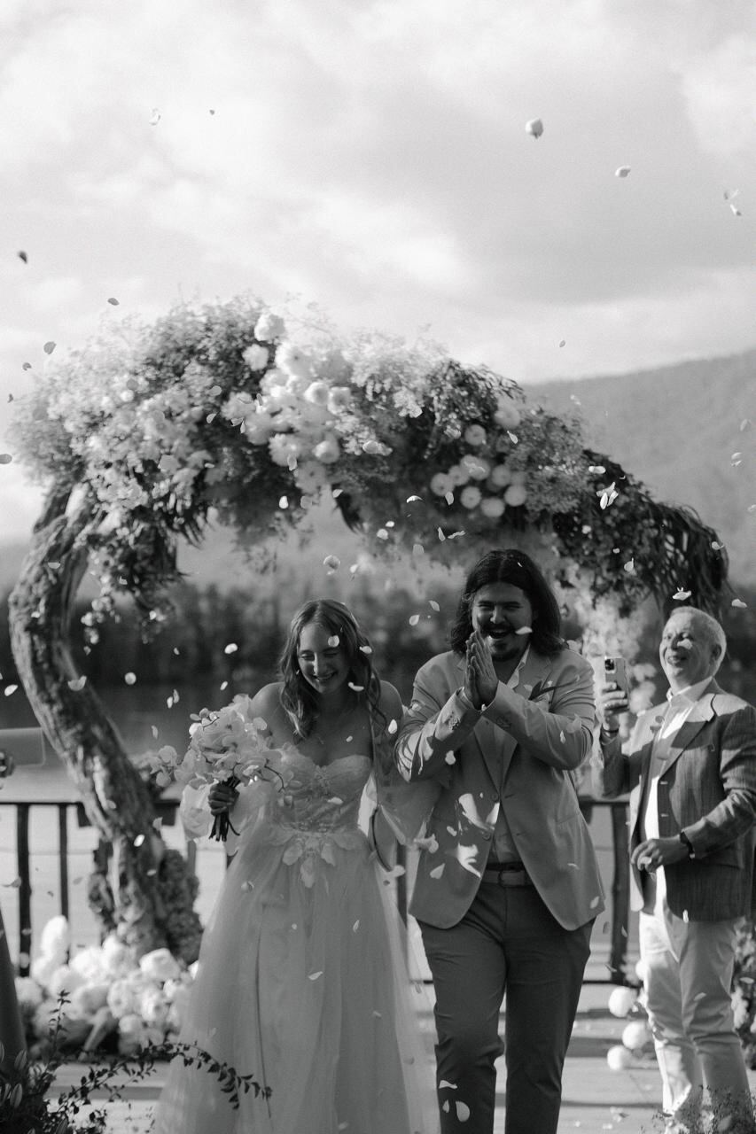 Black and white moment of the couple walking through a shower of petals